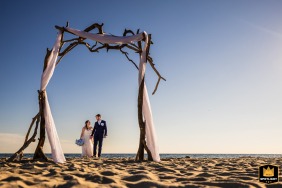 A couple walking beneath a driftwood arch at Bank Street Beach in Harwich, MA, wrapped in soft coastal light, capturing the simplicity and serenity of the seaside setting.